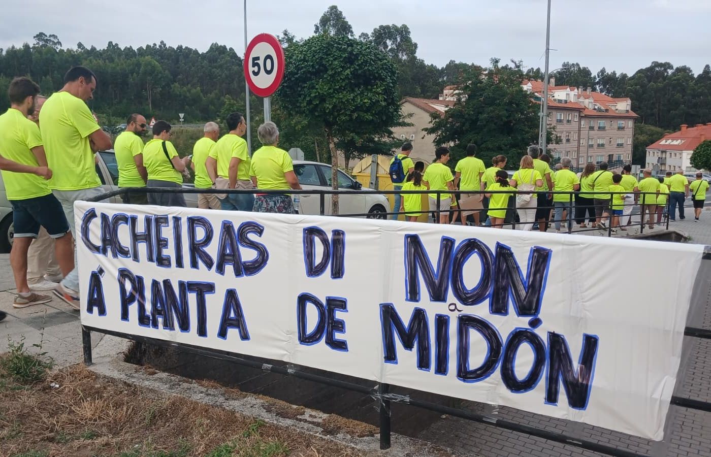 Pancarta feita a man co lema «Cacheiras di non á planta de Midón» e unha fileira de veciñas e veciños con camiseta amarela.