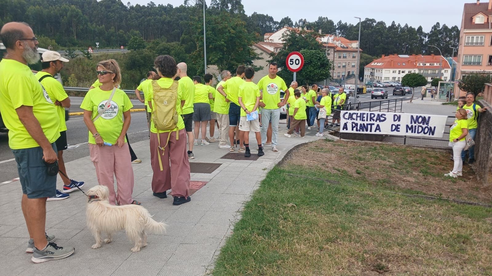 Veciñas e veciños con camiseta amarela concentrados na beirarrúa, a carón da estrada.