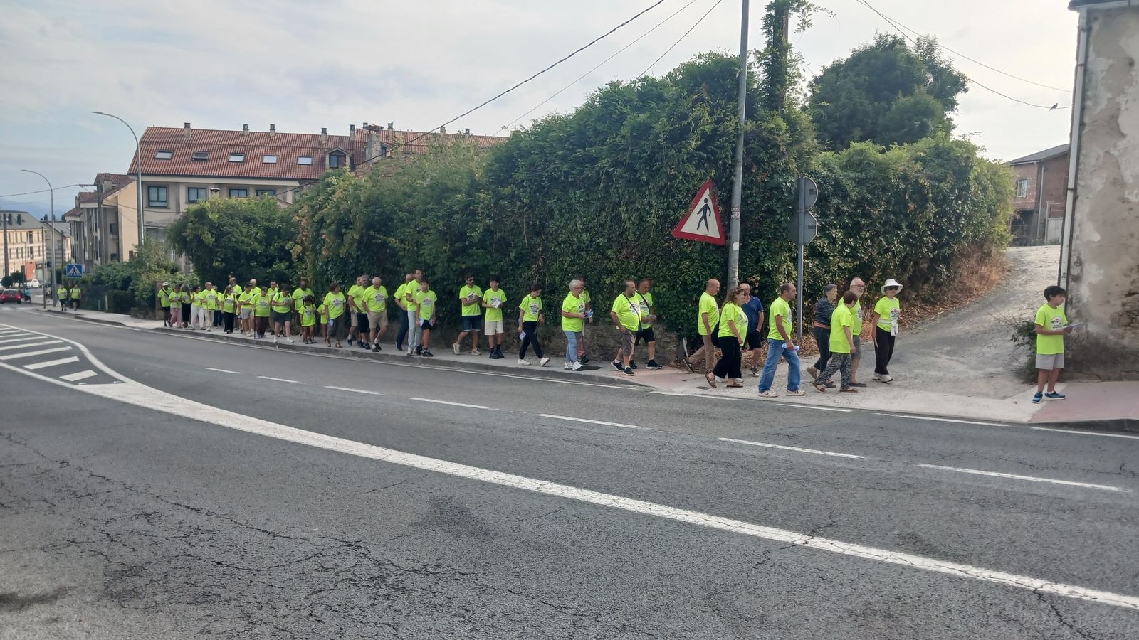 Longa fileira de veciñas e veciños con camiseta amarela camiñando pola beirarrúa.